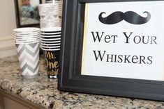 there is a sign that says wet your whiskers on the counter next to cups