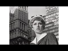 a black and white photo of a woman standing in front of tall buildings