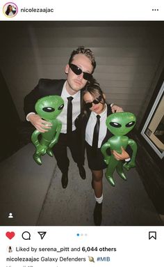 two people dressed in suits and sunglasses holding alien balloons while standing next to each other