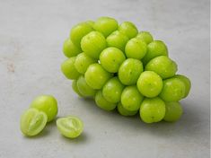 a bunch of green grapes sitting on top of a white counter next to two pieces of fruit