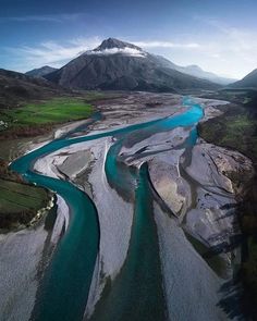 an aerial view of a river running through a mountainous area with snow capped mountains in the background