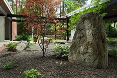 a large rock sitting in the middle of a yard next to a tree and bushes