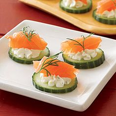 cucumbers with smoked salmon and cream cheese are on a white platter next to a glass of water