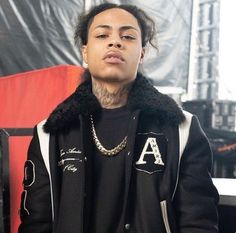 a young man wearing a black jacket and gold chain is standing in front of a stage