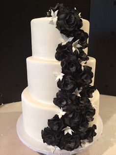 a three tiered white cake with black flowers