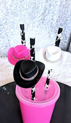 three hats are placed on top of each other in pink cups with black and white straws