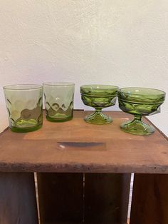 three green glass bowls and four glasses on a wooden table with a white wall in the background