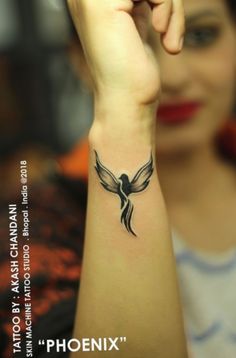 a woman is holding her arm up with a bird tattoo on it's wrist