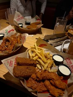 two baskets filled with fried chicken and french fries on top of a table next to drinks