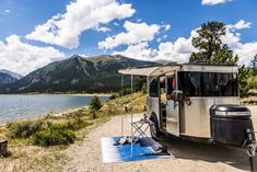 an rv parked next to a lake with mountains in the background