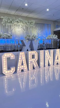 the letters are lit up in front of tables and chairs at a formal event with white flowers