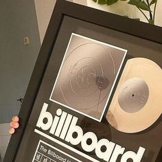 a person holding up a framed poster with a record on it's side and a plant in the background