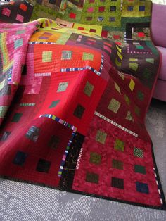 a couch with a quilt on top of it next to a pink chair and window