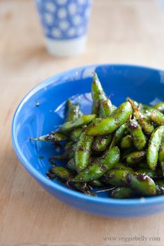 a blue bowl filled with green beans on top of a wooden table