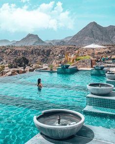 people are swimming in an outdoor pool with mountains in the background and blue skies overhead