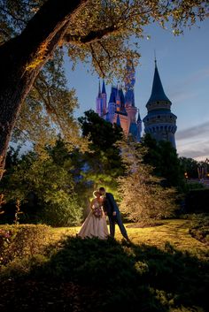 a bride and groom standing in front of a castle at night with the lights on