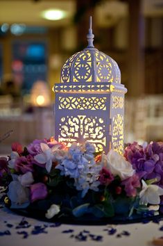 a white lantern sitting on top of a table next to purple and white flowers at night