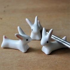 three white ceramic rabbits sitting on top of a wooden table next to a pen and pencil