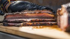 a person wearing black gloves and rubber gloves is slicing meat on a wooden cutting board