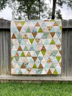 a patchwork quilt hanging on a fence in front of a wooden fence with green grass