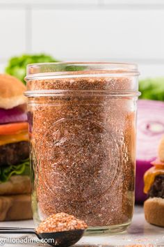 a jar filled with ground spices next to hamburgers