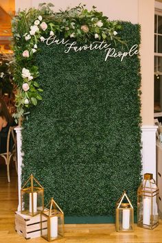 a green wall with white flowers and greenery on it, surrounded by candles in front of the sign