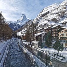 a river running through a snow covered mountain side town with tall buildings on both sides