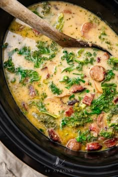 a crock pot filled with broccoli, sausage and spinach in cream sauce