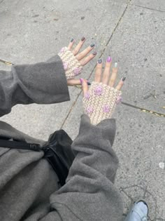 a woman's hands with pink and blue nail polish on them sitting on the sidewalk