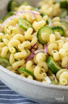 a bowl filled with pasta and cucumbers on top of a blue table cloth