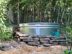 a large metal tub sitting on top of a pile of rocks next to a forest