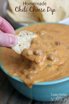 a hand dipping a tortilla chip into a bowl of homemade chili cheese dip