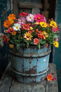 a bucket full of colorful flowers sitting on top of a wooden table next to an old door