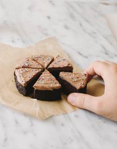 a hand holding a piece of chocolate cake with sprinkles