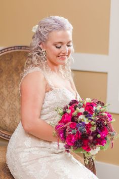 a woman in a wedding dress holding a bouquet on her lap and smiling at the camera