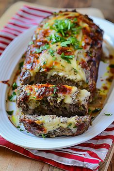 meatloaf with melted cheese and herbs on a white plate next to a red and white striped napkin