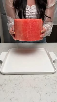 a woman holding a piece of watermelon on top of a white countertop