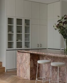 a kitchen with marble counter tops and stools next to a vase filled with flowers