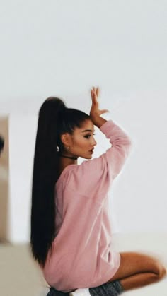 a woman with long hair sitting on the floor in front of a mirror wearing shorts and a pink sweater