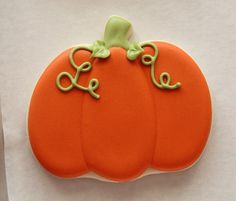 an orange decorated pumpkin cookie sitting on top of a piece of white paper with green icing