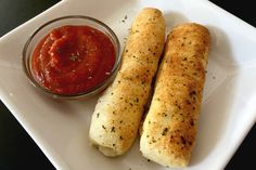 two breadsticks on a plate next to a small bowl of tomato dipping sauce