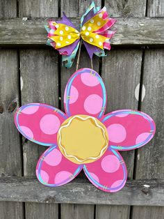 a pink and yellow flower with polka dots on it is hanging from a wooden fence