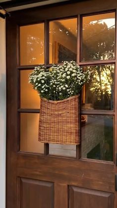 a basket with flowers hanging from the side of a wooden door, in front of a window