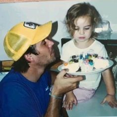 a man holding a child and looking at a birthday cake on a plate with candles