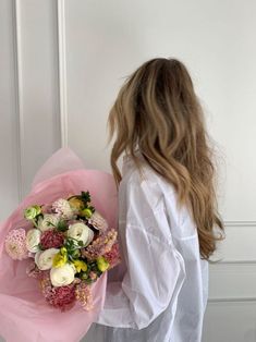 a woman holding a bouquet of flowers in front of a white door with pink and yellow accents