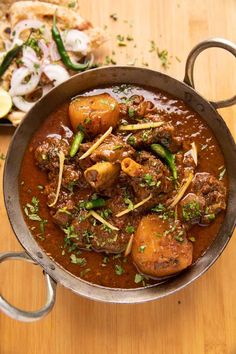 a pot filled with stew and vegetables on top of a wooden table next to bread