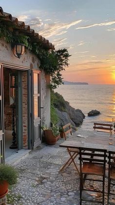 an outdoor dining area with table and chairs near the water at sunset or sunrise time