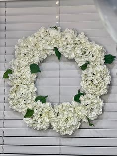 a wreath made out of white flowers sitting on top of a window sill next to blinds