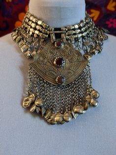 Vintage Kashmiri choker with a large pendant and loads of jingling accents. This is a vintage piece but has been polished so the metal has sheen. There are signs of age evident, most notably in the surface pattern and with non-matching dangles. Three carnelian cabochons, original and intact.  Lots of jingling accents that make a sound with movement. The sound not only announces your arrival, but wards off the evil eye as well.  Not including the ties, this is 11.75" across. The ties are 6" each Kashmiri Gold Jewellery, Ceremonial Meenakari Pendant Jewelry, Kashmiri Jewellery Vintage, Kashmiri Tilla Embroidery Pheran, Ceremonial Meenakari Brass Necklace, Silversmithing Jewelry, Afghan Jewelry, Choker Pendant, Aesthetic Photography Grunge