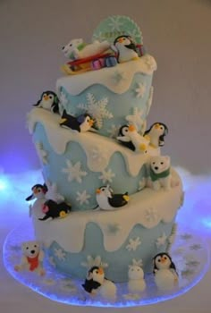 a three tiered cake with penguins and snowflakes on the bottom, in blue frosting